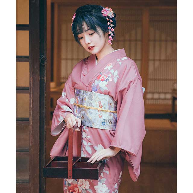 Woman in a pink floral kimono sitting in a traditional Japanese room.
