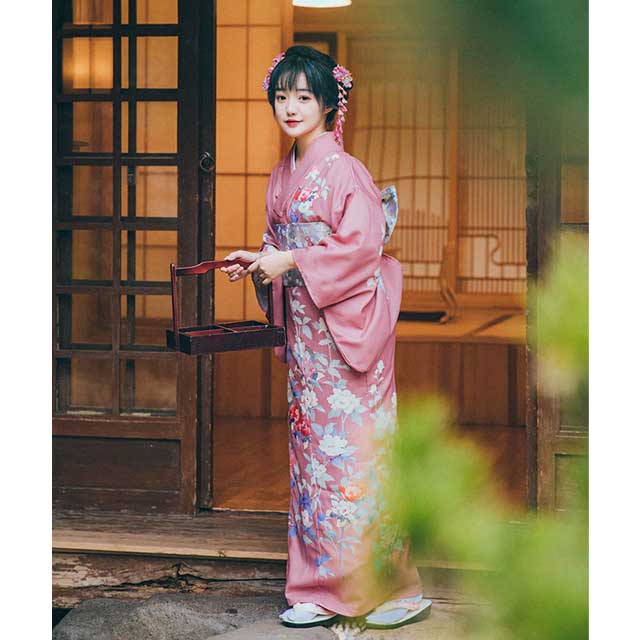 Woman in a pink floral kimono sitting in a traditional Japanese room.
