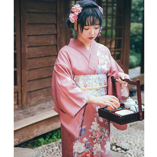 Woman in a pink floral kimono sitting in a traditional Japanese room.