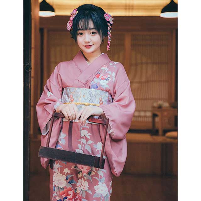 Woman in a pink floral kimono sitting in a traditional Japanese room.