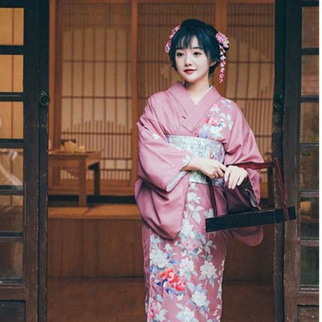 Woman in a pink floral kimono sitting in a traditional Japanese room.